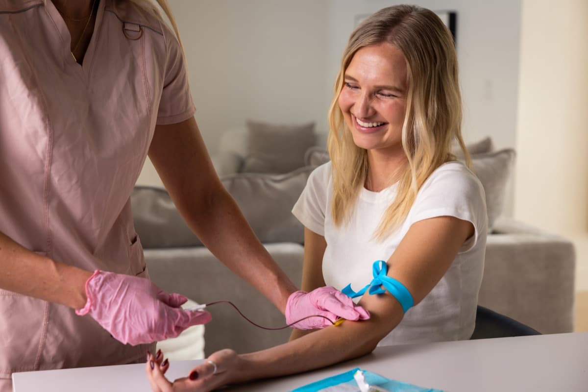 Phlebotomist drawing blood from a smiling patient at home