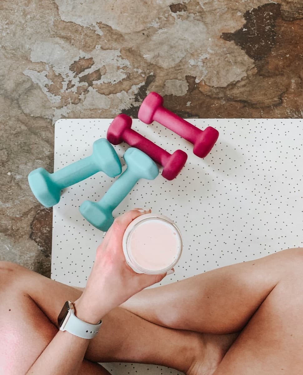 Dumbbells and a protein shake on a yoga mat